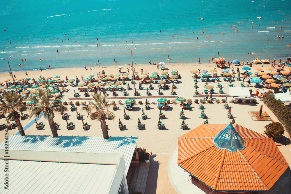 Aerial view to the sandy beach with many people and umbrellas, beach bar and turquoise color Adriatic Sea water.