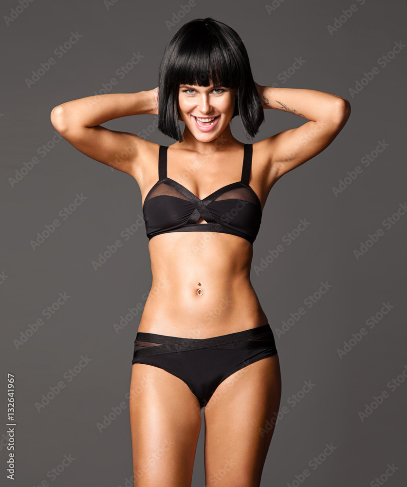 Woman with beautiful athletic tanned body and short haircut bob posing on gray background and looking at the camera
