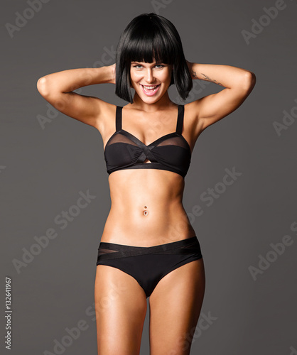 Woman with beautiful athletic tanned body and short haircut bob posing on gray background and looking at the camera © deniskomarov