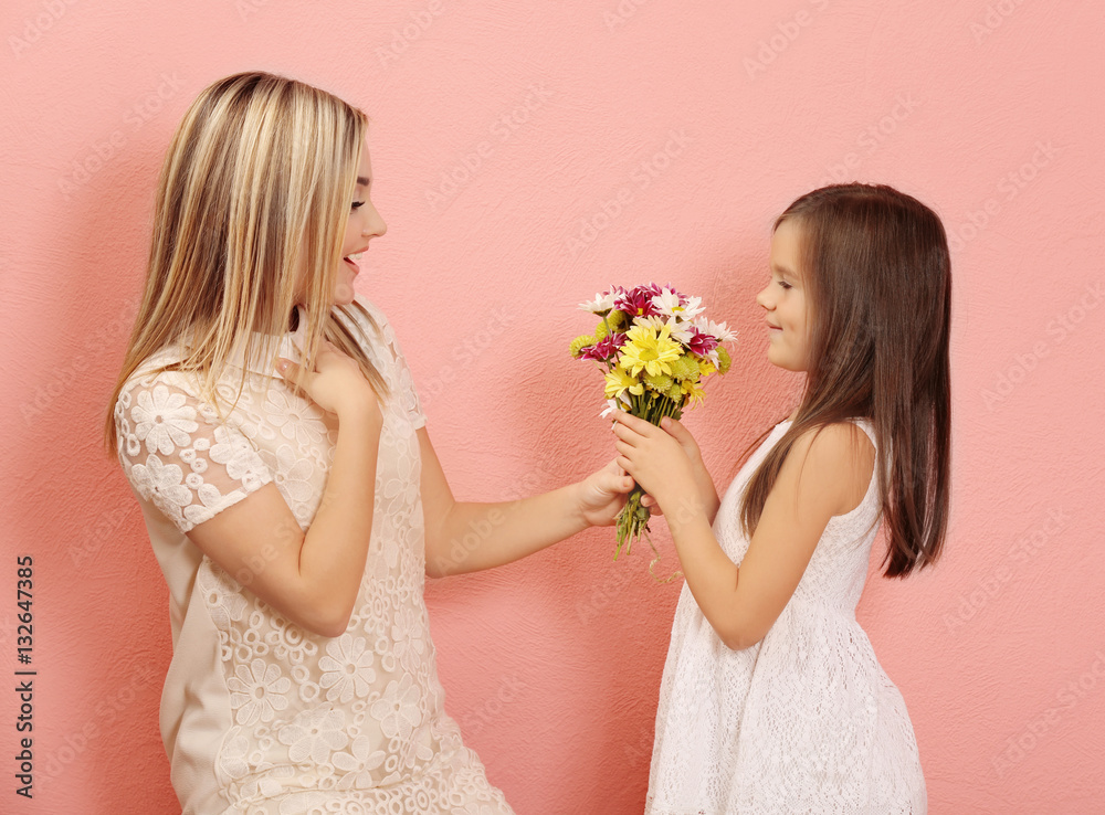 Little girl giving bouquet of flowers to her mother, on color background. Mother's day concept