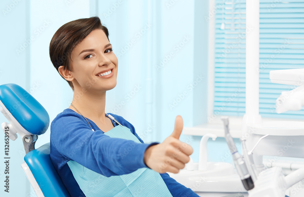 Young female patient visiting dentist office.Beautiful smiling woman with healthy straight white teeth sitting at dental chair and making thumbs up.Dental clinic.Stomatology Young female patient visiting dentist office.Beautiful smiling woman with healthy straight white teeth sitting at dental chair and making thumbs up.Dental clinic.Stomatology