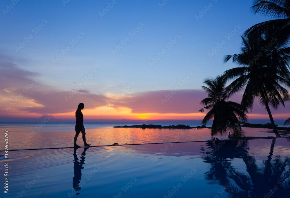 Woman silhouette walking over infinity pool at sunset in Koh Phangan, Thailand Woman silhouette walking over infinity pool at sunset in Koh Phangan, Thailand