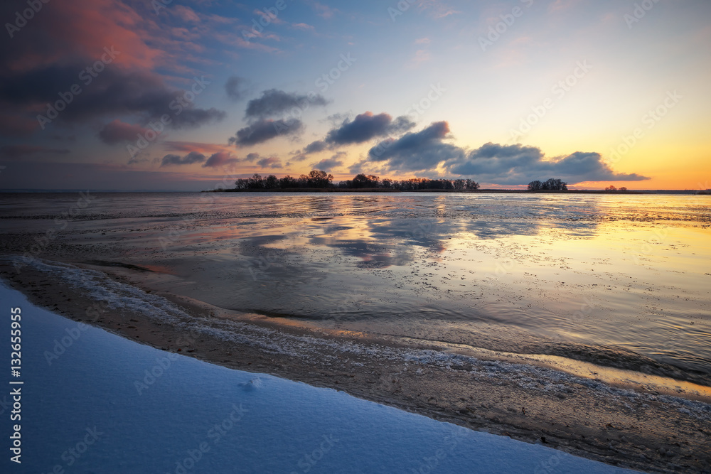 Winter landscape with frozen lake and sunset sky. 