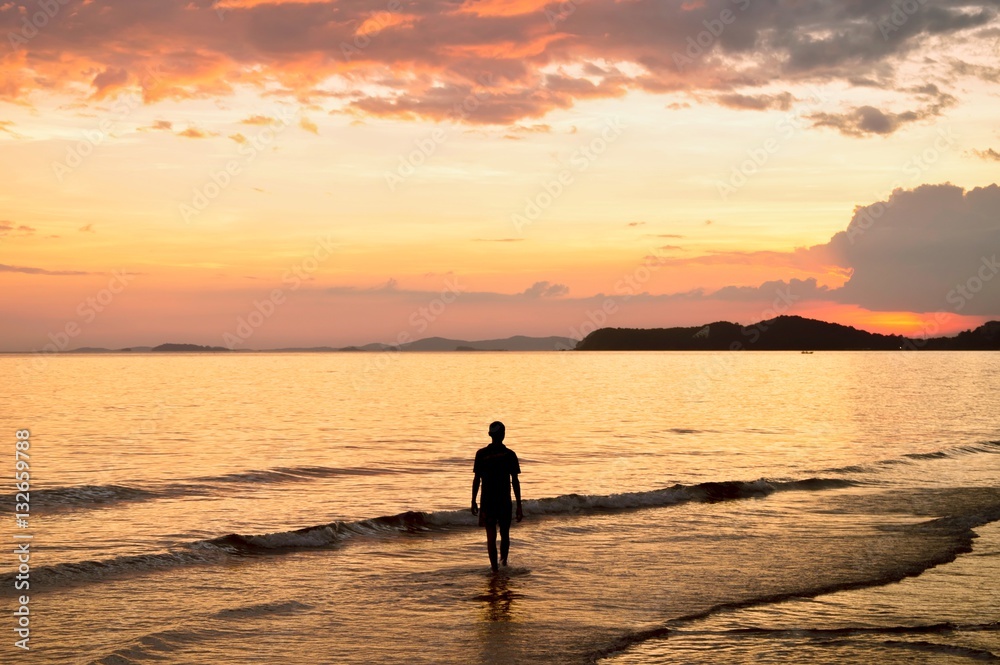 Silhouette of lonely man walking in to the sea at sunset