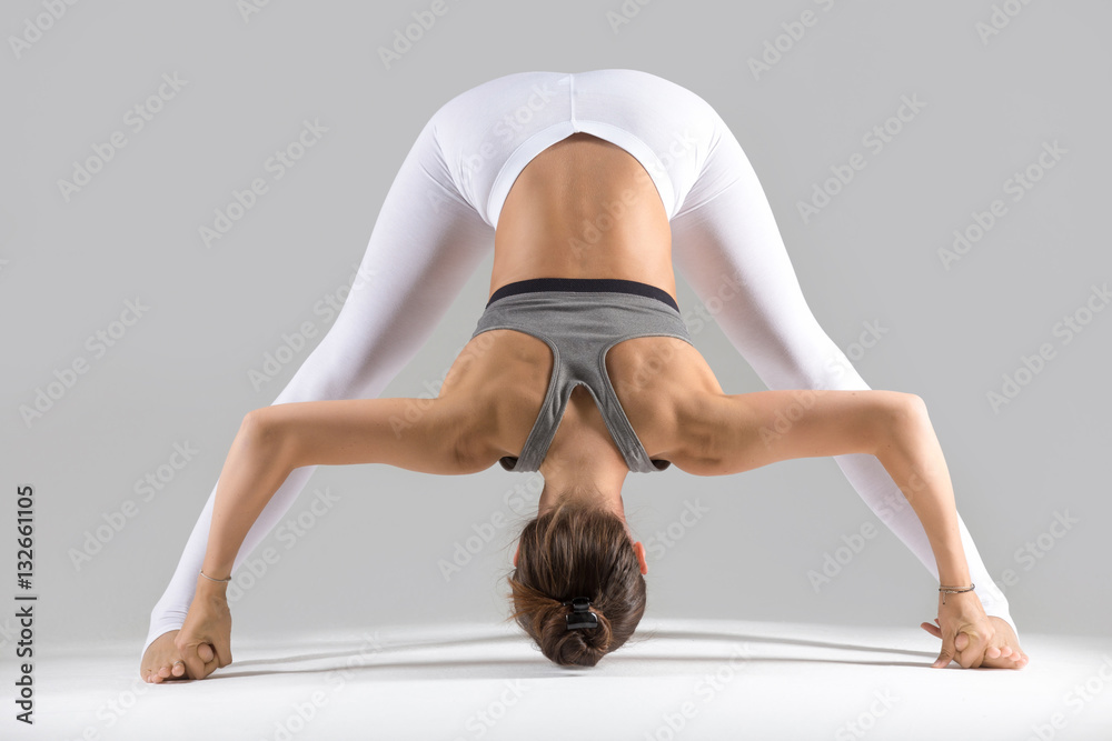 Young attractive woman practicing yoga, standing in Wide Legged Forward Bend  exercise, Prasarita Padottanasana pose, working out wearing sportswear,  indoor full length, grey studio background Stock Photo | Adobe Stock
