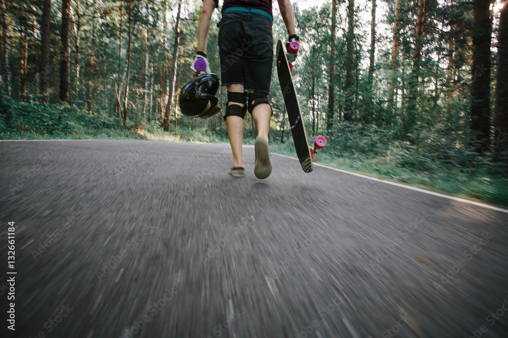 Obraz premium Young man with longboard is back on the road in the forest. Phot