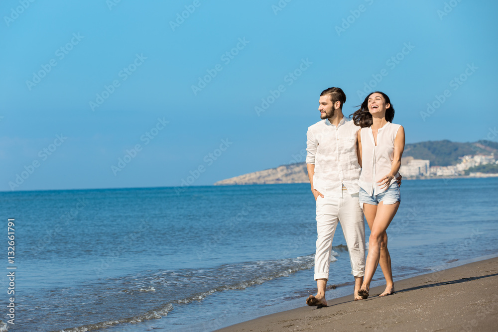 Couple walking on beach. Young happy interracial couple walking on beach smiling holding around each other.