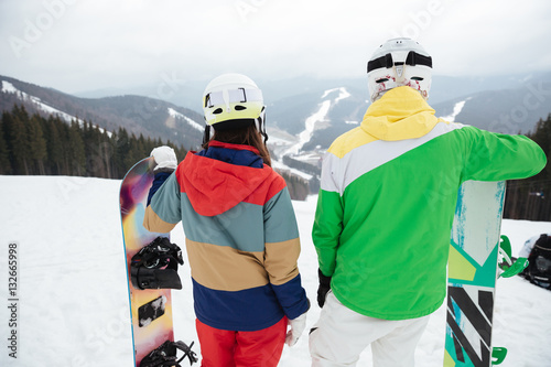 Back view photo of young loving couple snowboarders