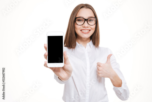 Smiling business woman in eyeglasses showing blank smartphone screen