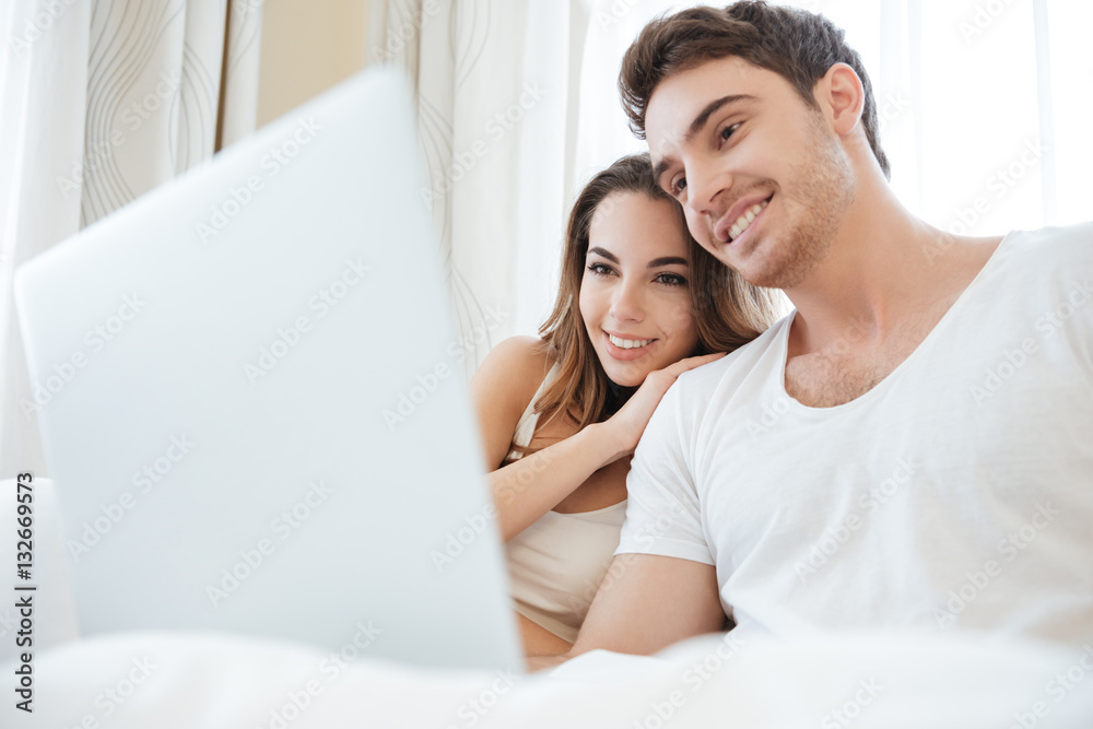 Cheerful young couple using laptop in bed Cheerful young couple using laptop in bed