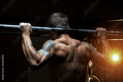 Strong muscular man doing pull up exercise in gym