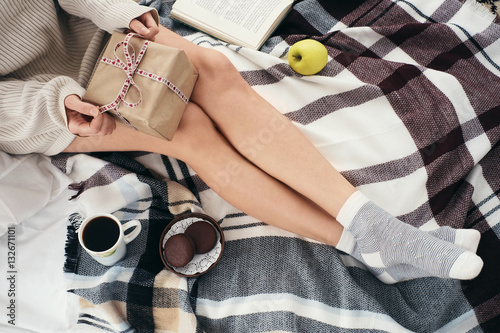 Soft cozy photo of woman in warm sweater on the bed with a gift