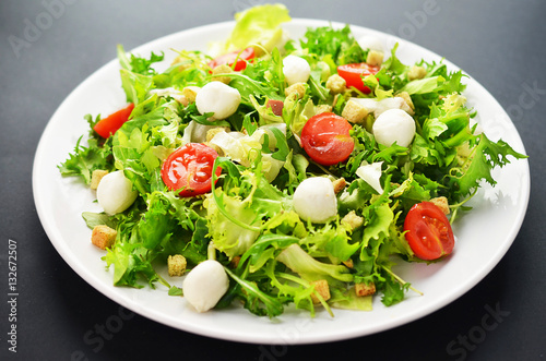 Fresh salad on a white plate on a black table.