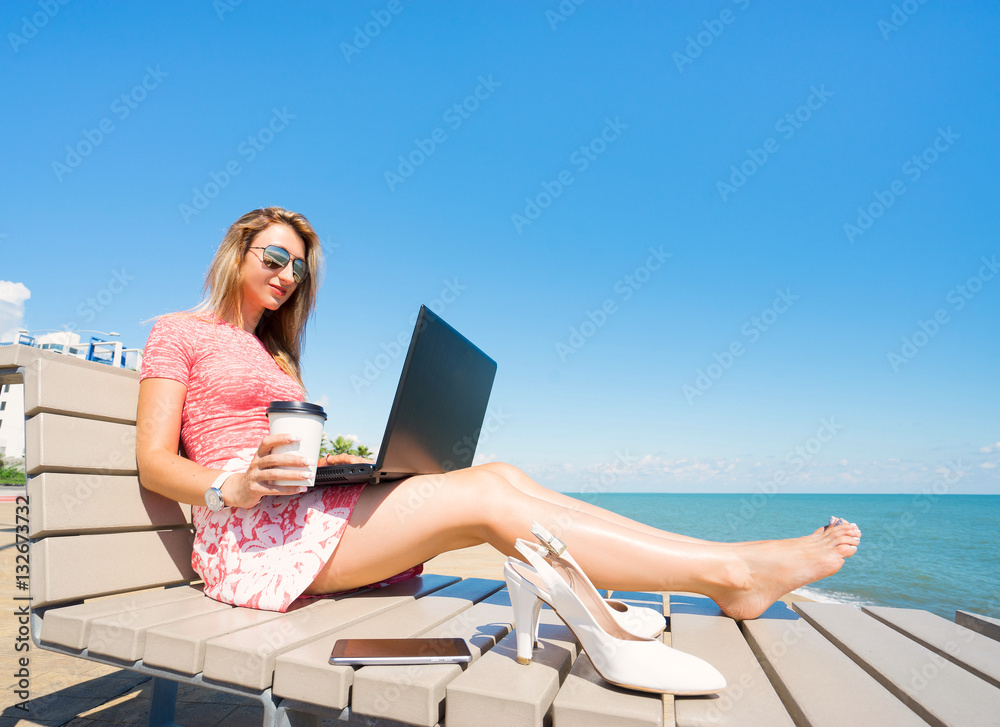 Young beautiful woman sitting on the beach chiar  with laptop , smartphone and shoes, and drink coffee.