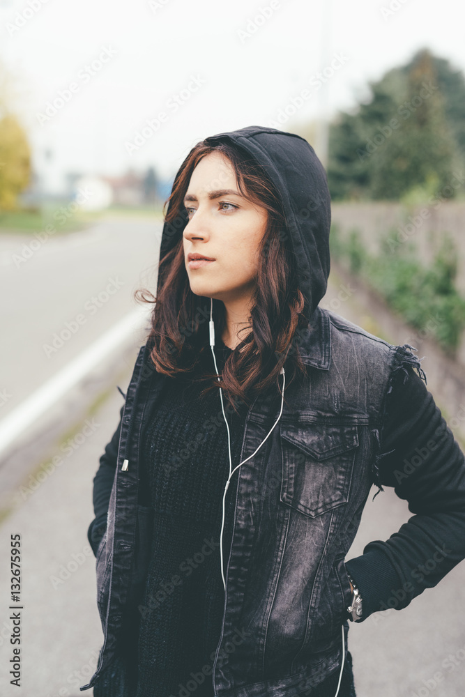 Fototapeta premium Young beautiful eastern woman posing outdoor in the city listening music with earphones - music, technology, relaxing concept