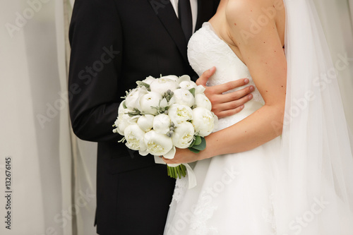 Wedding couple, bride and groom hugging at wedding ceremony, close-up peony bouquet in bride hand. Wedding concept
