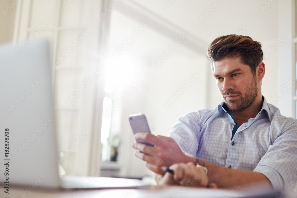 Relaxed young man sitting at desk using mobile phone