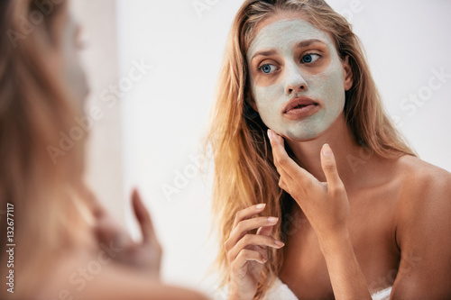 Woman looking in the mirror with face mask photo