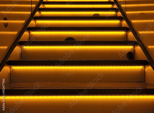An illuminated or neon-colored stairway, striking background with yellow and orange colors. Funny mouseholes and led lighting.