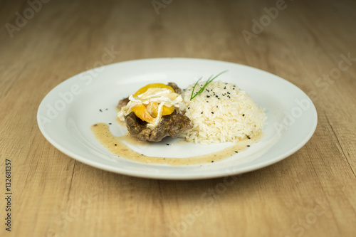 Meat with peaches and rice on plate on wooden table