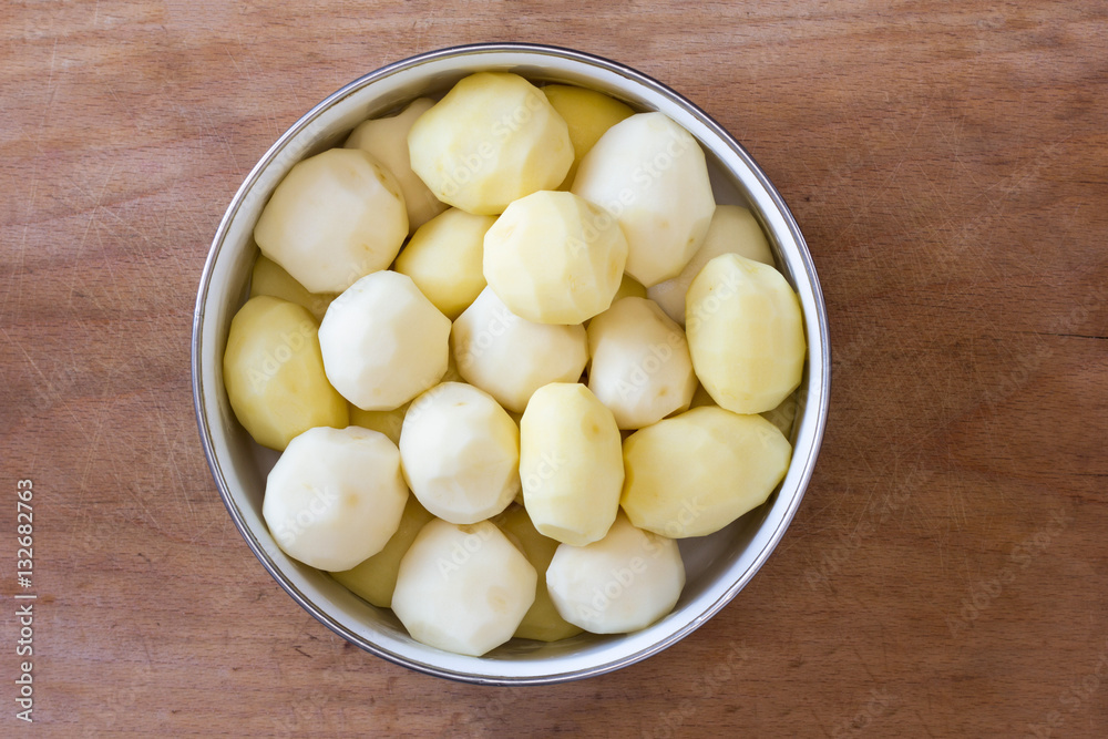 raw peeled potatoes in a circular bowl on an old rustic wooden table closeup, top view raw peeled potatoes in a circular bowl on an old rustic wooden table closeup, top view