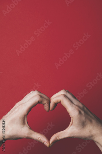 Female hands creating the shape of a love heart over a red background. Romance and valentines day concept