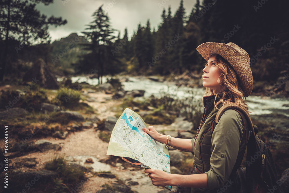 Fototapeta premium Woman hiker, searching right direction on map near wild mountain river