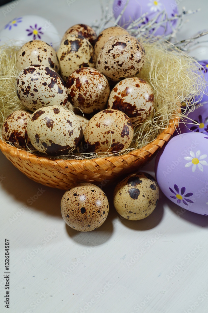 Quail eggs in a wicker basket and colorful Easter eggs on a grey  background - Easter decoration

