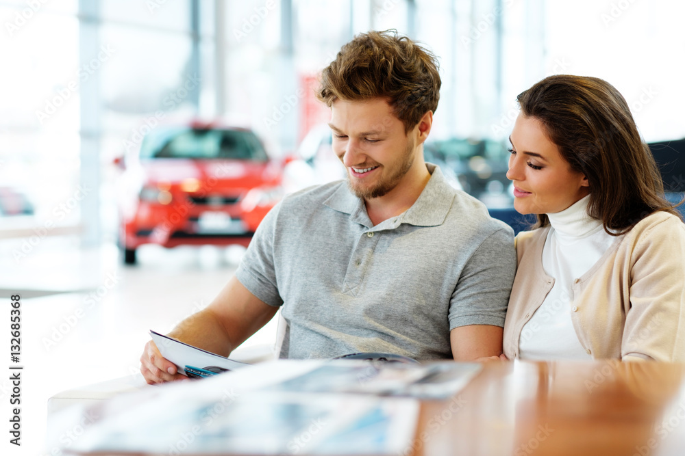 Fototapeta premium Beautiful young couple reading a booklet at the dealership showroom