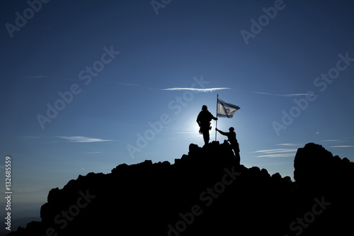Canvas Print Two soldiers raise the Israeli flag on top of the mountain