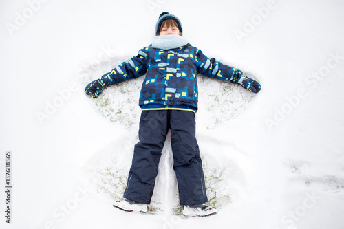 Little sweet child, boy, lying on north pole snow, making snow a