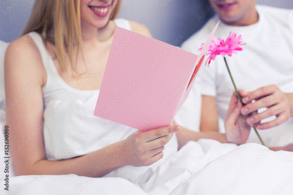 close up of couple in bed with postcard and flower close up of couple in bed with postcard and flower