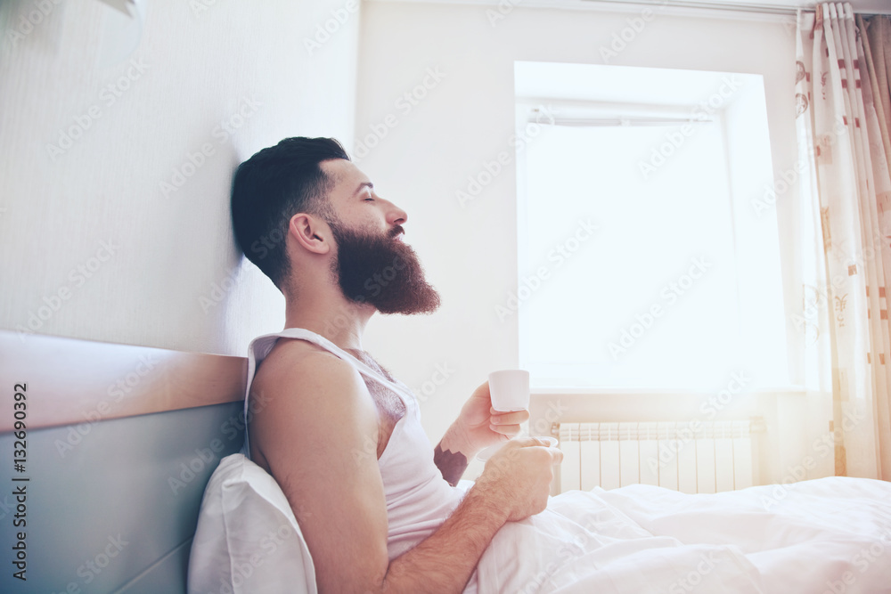 Bearded man in bed drinking morning espresso coffee in sunrise l Bearded man in bed drinking morning espresso coffee in sunrise l