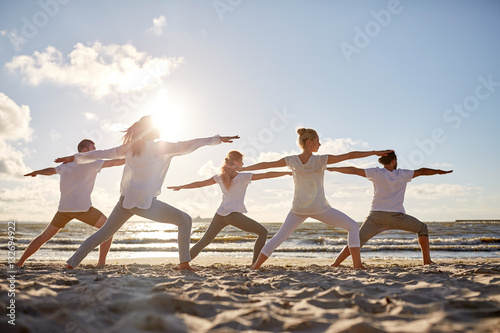 group of people making yoga exercises on beach photo
