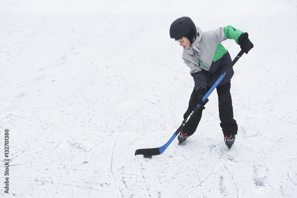 Fototapeta premium Child boy playing ice hockey at the skating rink outside in winter.