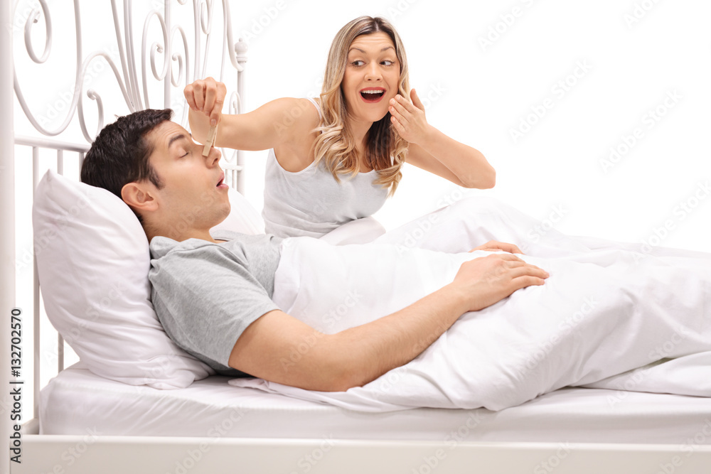 Man snoring next to woman putting clothespin on his nose Man snoring next to woman putting clothespin on his nose