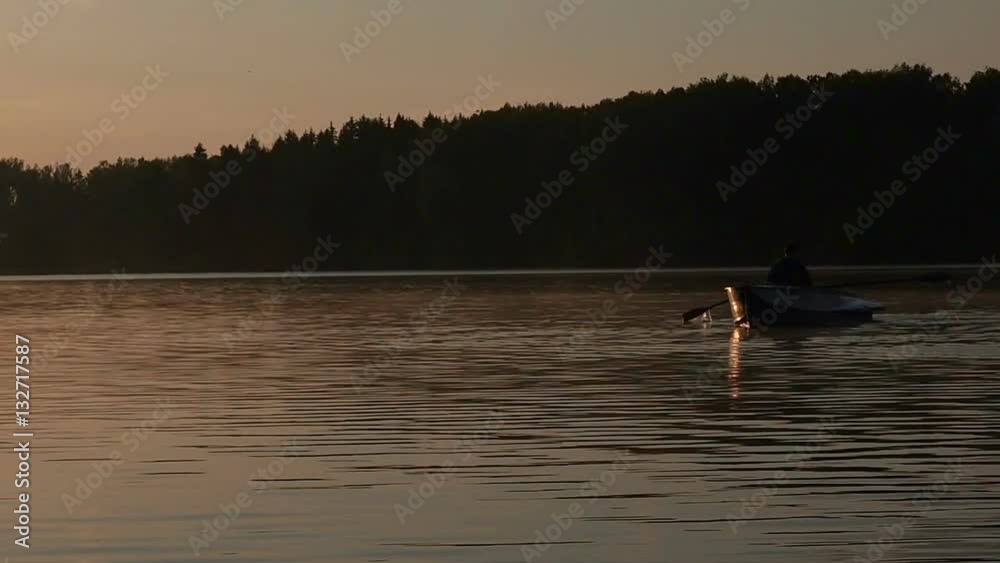 Alone man riding on a rowing boat on the lake dusk time. Golden sunset sunrise on the lake. Leisure nature concept Alone man riding on a rowing boat on the lake dusk time. Golden sunset sunrise on the lake. Leisure nature concept