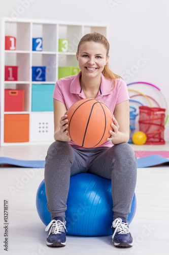 Woman sitting on exercise ball and holding basketball