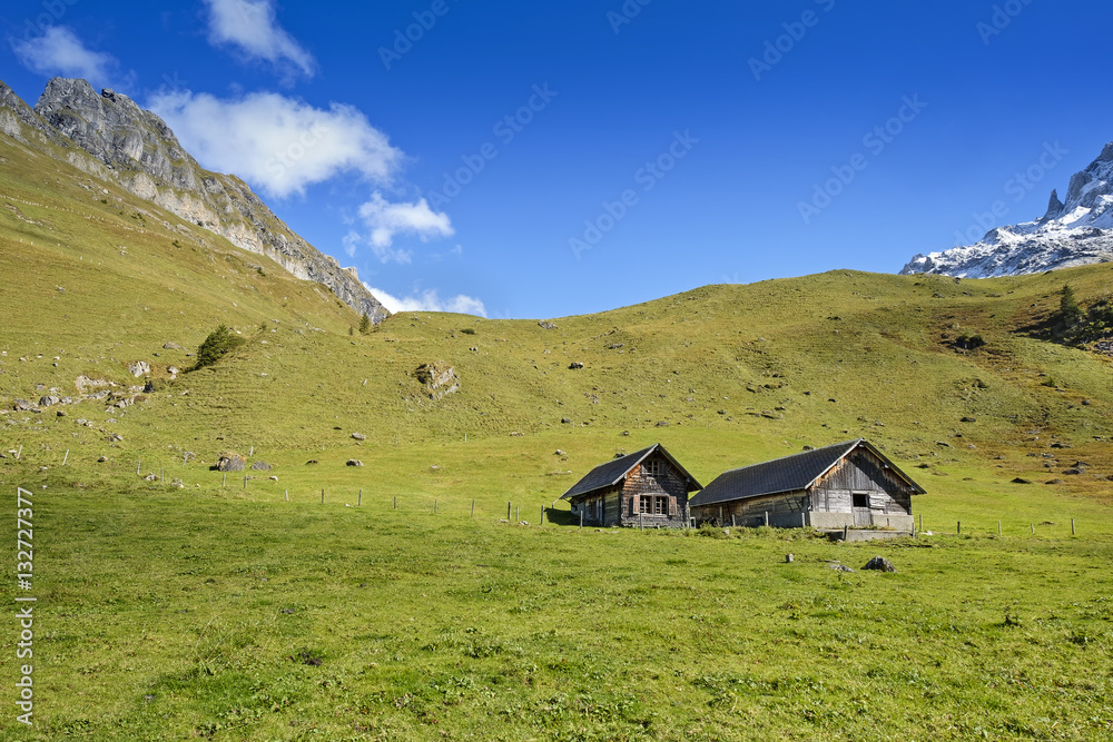 Mountain huts with view over green meadow and mountain peaks Mountain huts with view over green meadow and mountain peaks