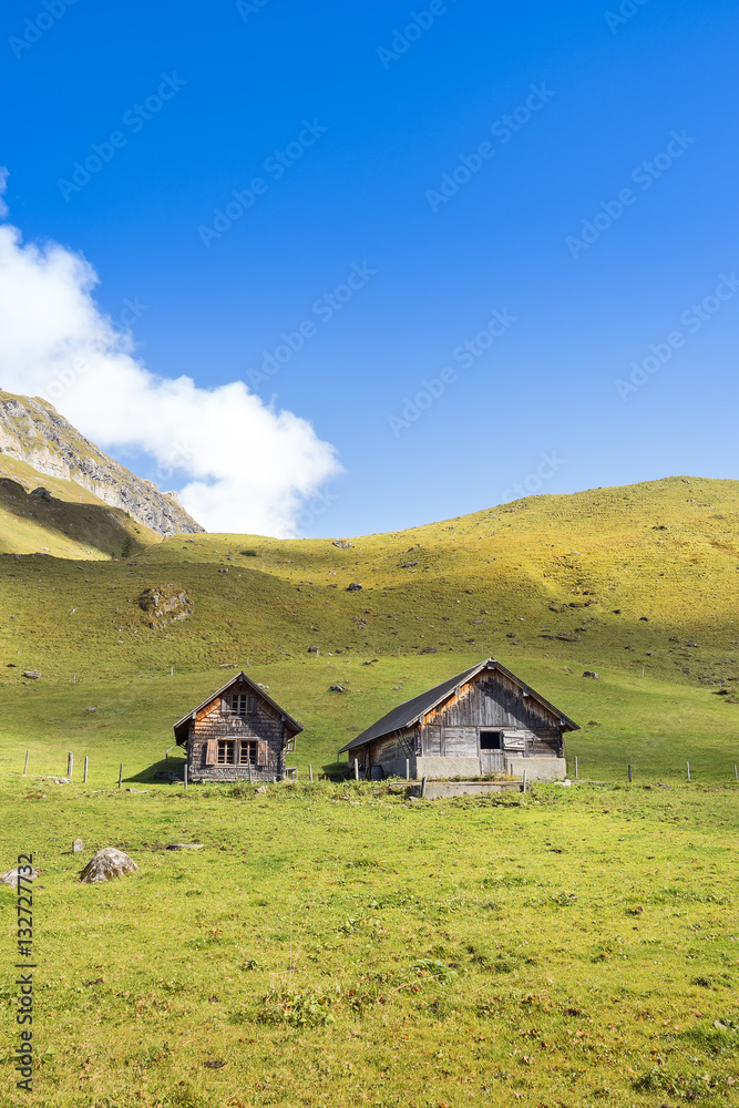 Mountain huts with view over green meadow and mountain peaks Mountain huts with view over green meadow and mountain peaks