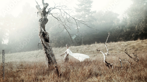 woman in foggy field next to old tree