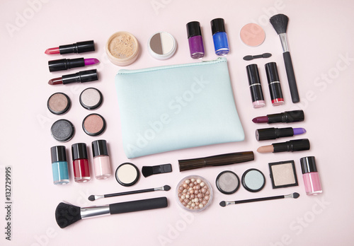 A selection of cosmetic beauty products arranged around a blue make up bag on a pastel pink background