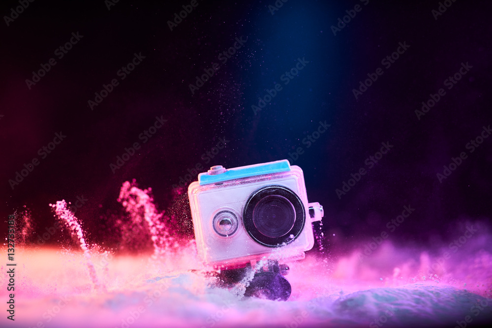 Obraz premium Concept: gear, gadget, action lifestyle, millennial. Vivid colorful shot of action camera in waterproof case fall dropped in powder sand. Time freeze.