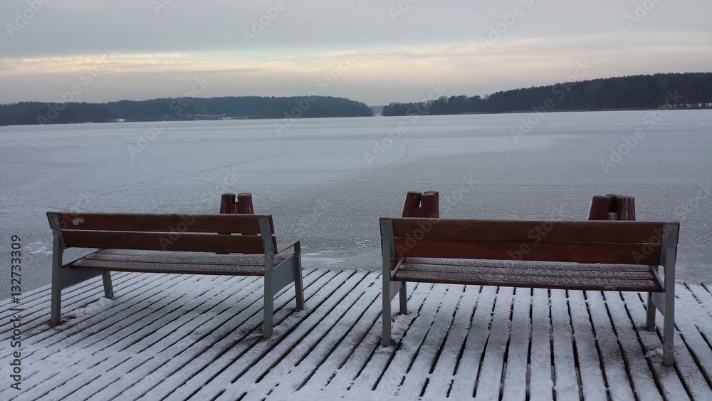 Two benches on the wooden pier on the frozen lake on a cloudy day