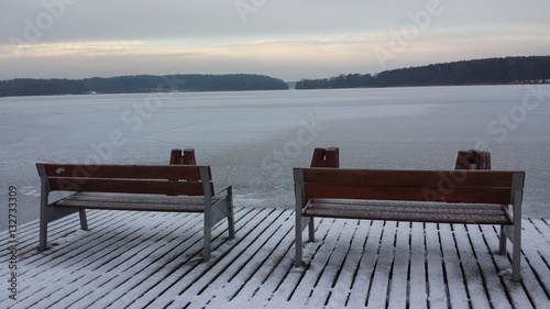 Two benches on the wooden pier on the frozen lake on a cloudy day © abrada