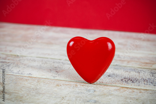 Closeup of red heart figure on wooden table in red background