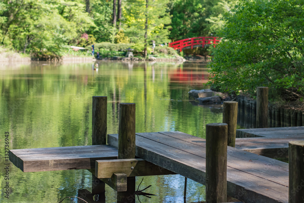 Japanese gardens with reflection pond, red bridge, and wood boardwalk.