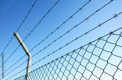 Obraz na plátně Coiled razor wire with its sharp steel barbs on top of a mesh perimeter fence en