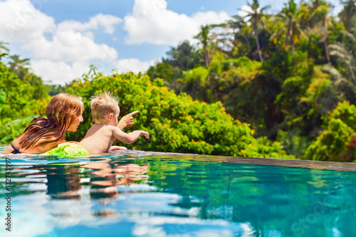 Family Bali beach holiday concept. Happy son with mother - active baby at poolside in infinity swimming pool. Summer healthy lifestyle and children water activity, games and lessons with parents. © Tropical studio