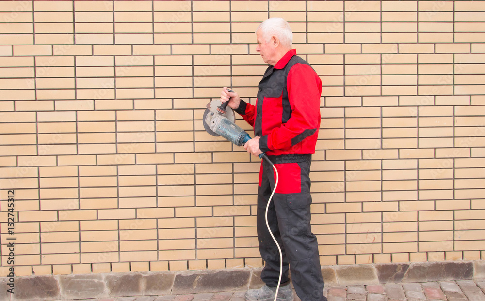A worker stands near a brick wall with grinder. Place for text. A worker stands near a brick wall with grinder. Place for text.